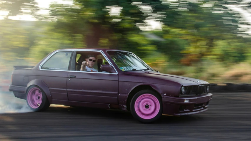 a purple car traveling down a road next to trees