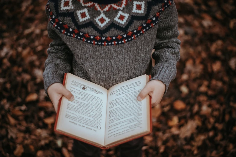 a person holding a book in the middle of some leaves