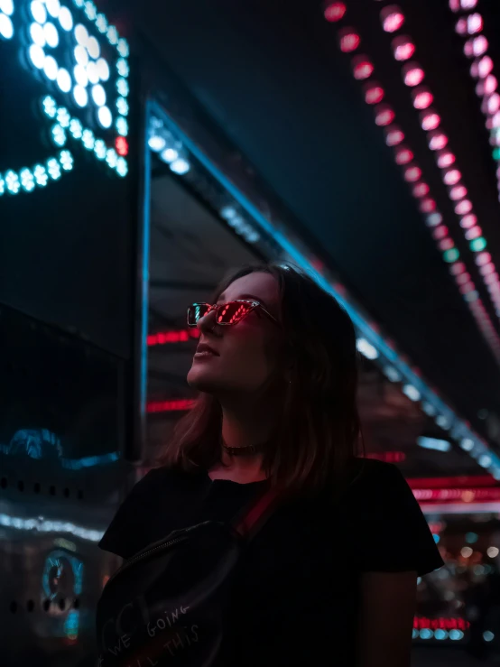 a young woman wearing sunglasses standing in front of an illuminated clock