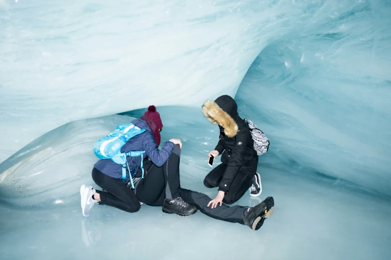 two young women sitting next to each other in front of a snow cave