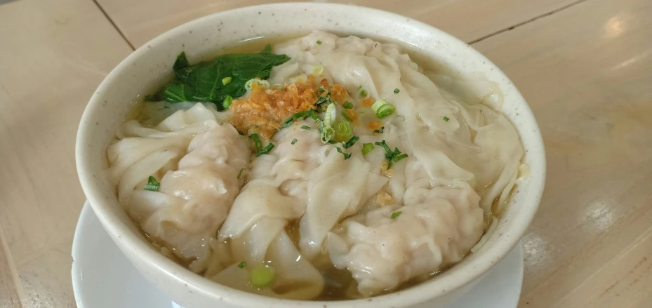 soup with noodles and meat in bowl with sauce and a green garnish