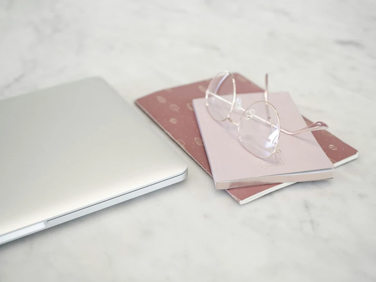 a pink notebook with glasses on top of it next to a silver laptop computer