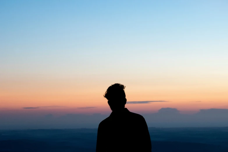 a man stands before a sunset with his hair in the air