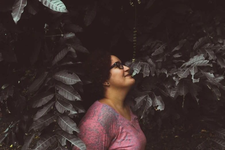 a woman standing between two green trees looking up at the sky