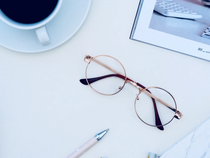 a cup of coffee sits near a pair of glasses and other office supplies