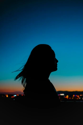 the silhouette of a girl in front of a city skyline at night