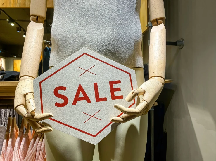 a mannequin holding a white sale sign with red sale written on it