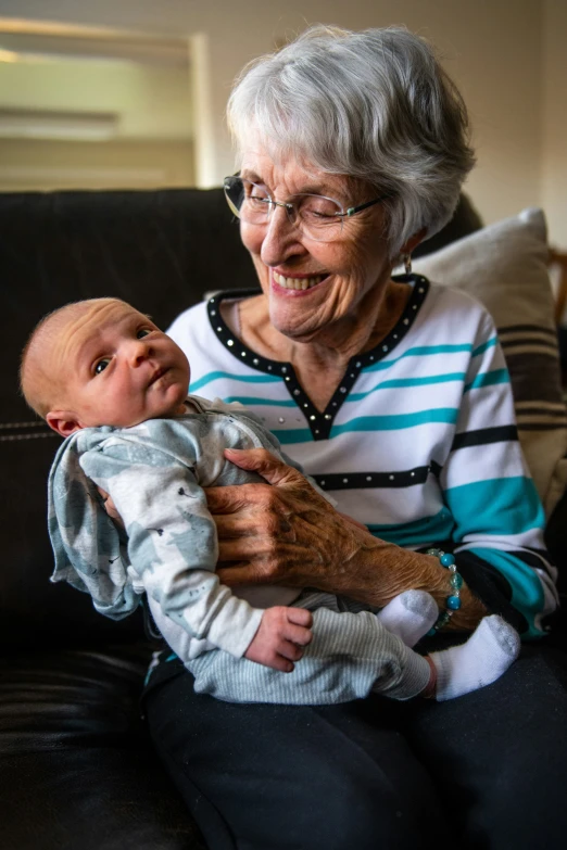 an older woman holding a baby while sitting on a couch