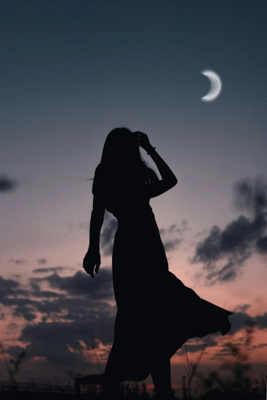 silhouetted woman standing on beach watching moon during sunset