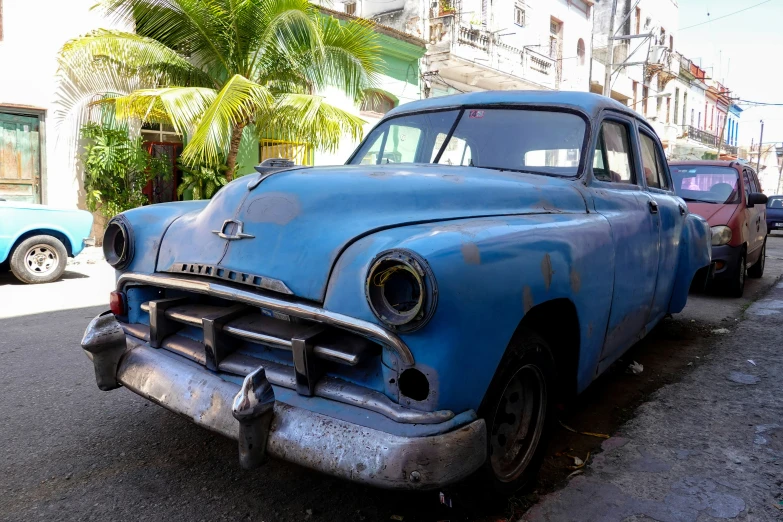 an old blue car is sitting in the street