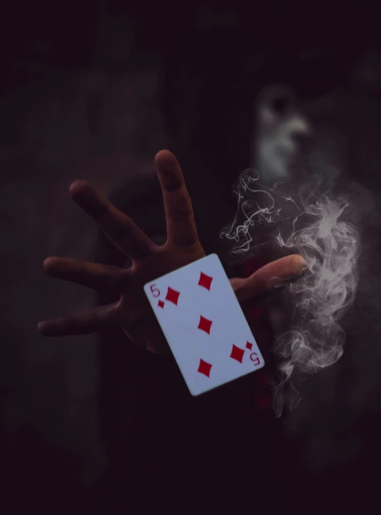 a hand holding a playing card with a smoking cigarette