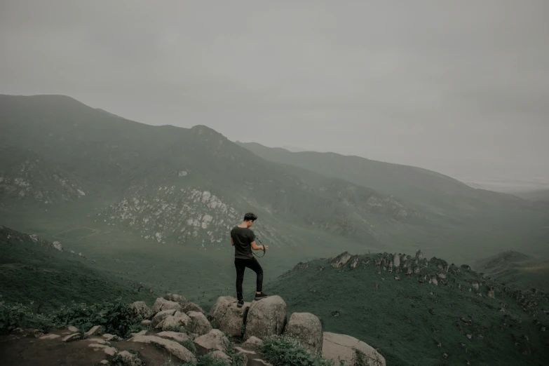 a man in grey hoodie standing on rocks near mountains