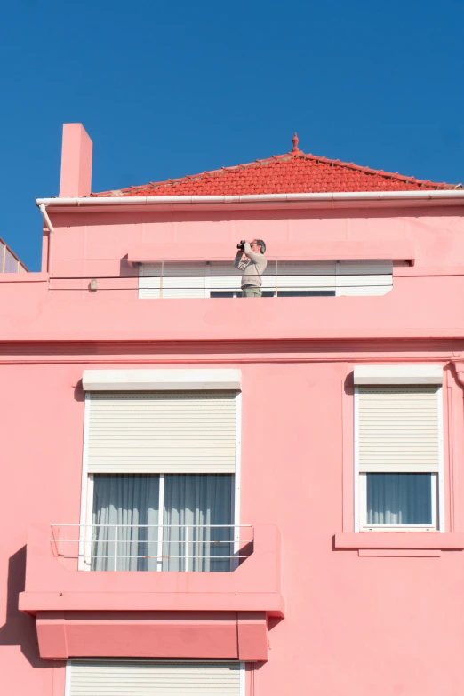 a person standing on top of the roof of a pink building