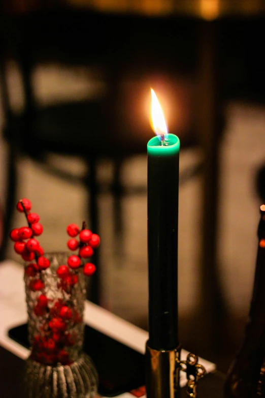 a black candle in a clear vase with red berries on it
