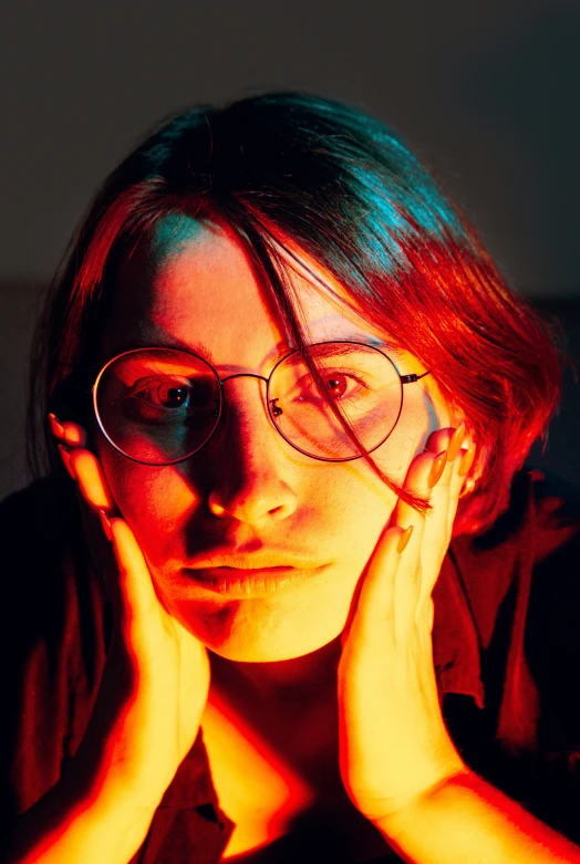 woman in glasses and dark shirt poses with hands on her face