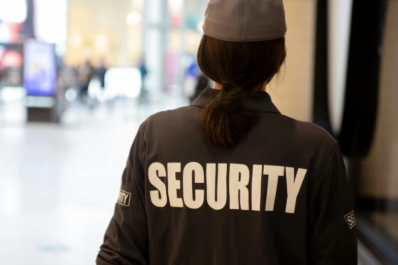 the back of a woman walking in an airport wearing a security sweatshirt