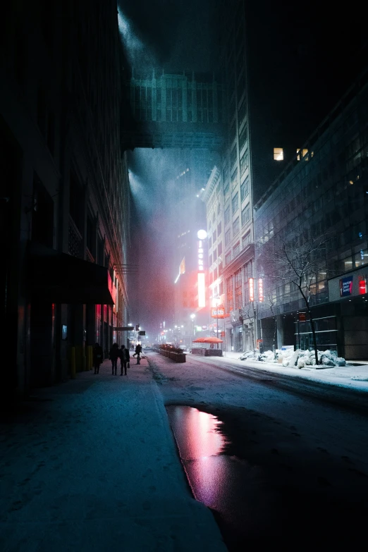 the night scene shows people on a snowy sidewalk in the city