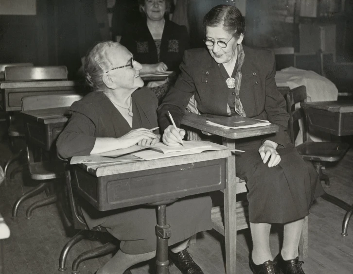 two women sitting at a desk writing in front of an instructor