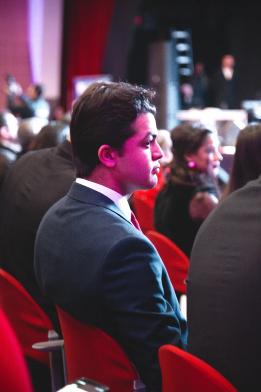 a man is sitting on a red chair in front of an audience