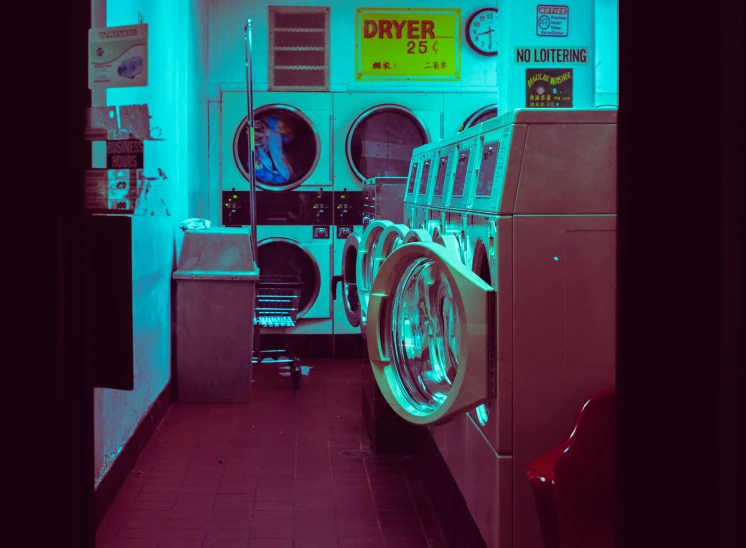 a row of washers and dryer machines sit in a blue hued room