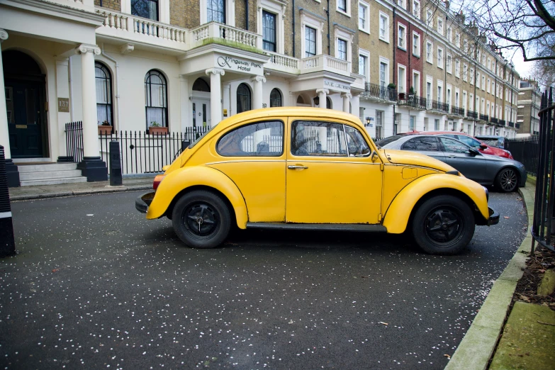 a yellow beetle sitting in the street near a building