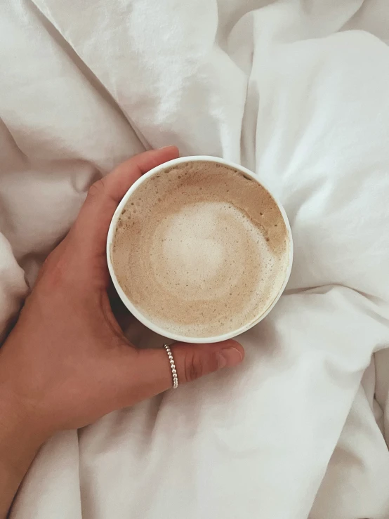 someones hand holding a cup of coffee and blanket