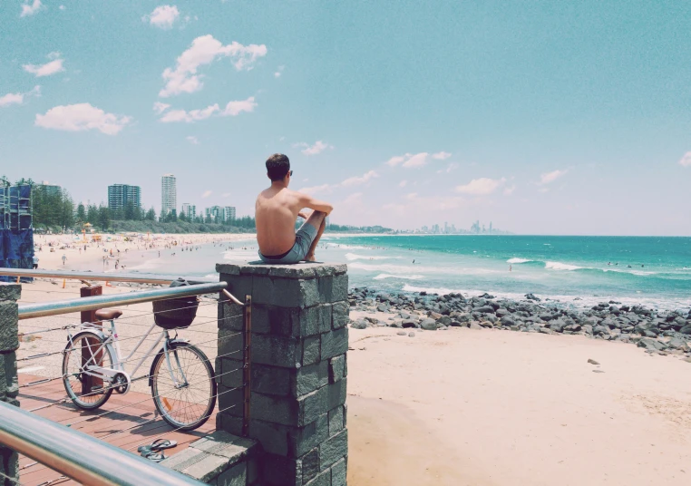 the man sits on the railing over looking the ocean