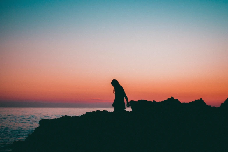 a woman walking along the shore line during a sunset