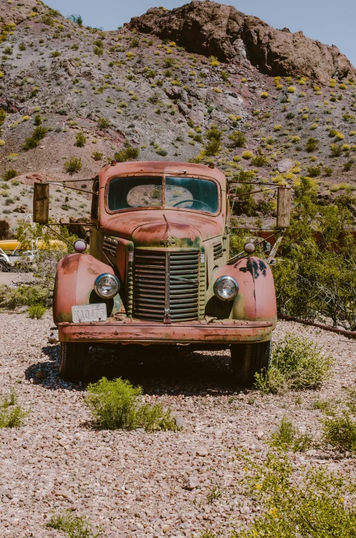 an old rusty truck sits on the side of a dirt road