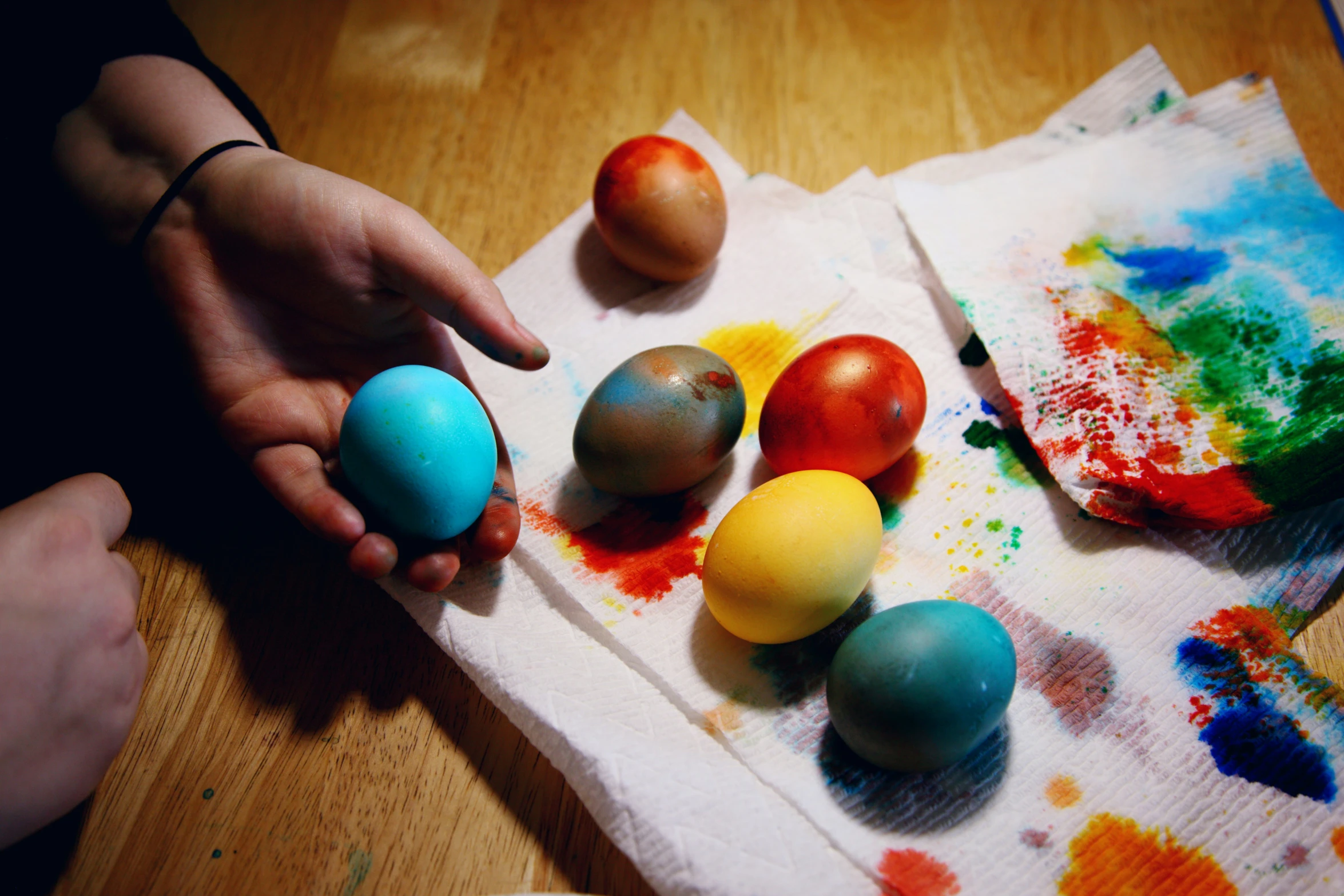 an image of a person's hand pointing toward painted eggs