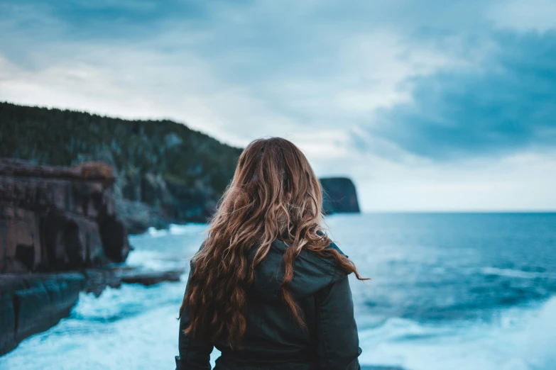 a person with long hair looking out into the ocean