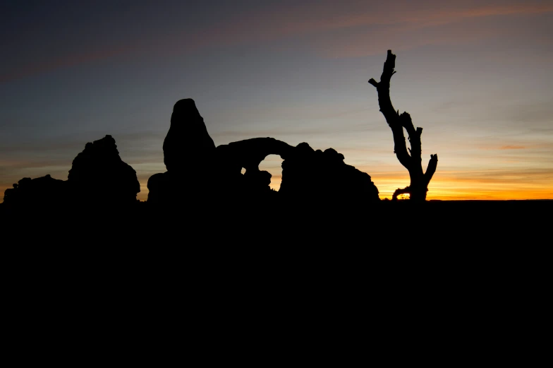 silhouettes of rocks and trees against an orange sky