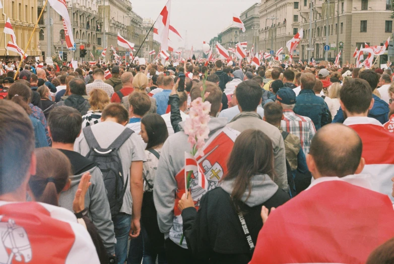a crowd of people with red and white flags walking along a street