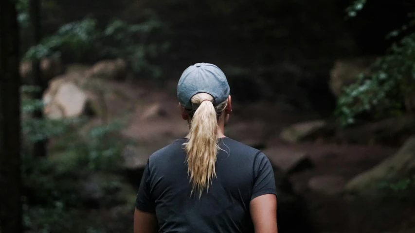 a woman with a pony tail, black shirt and shorts standing in the forest