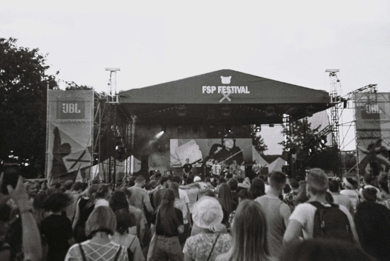 a crowd of people walk past a large stage set up with an awning