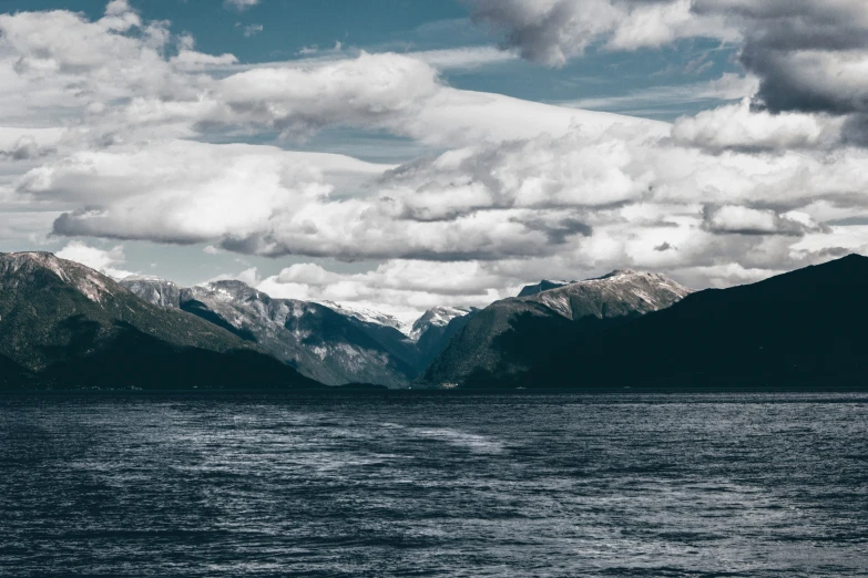 mountain peaks rise out from the water beneath a partly cloudy sky