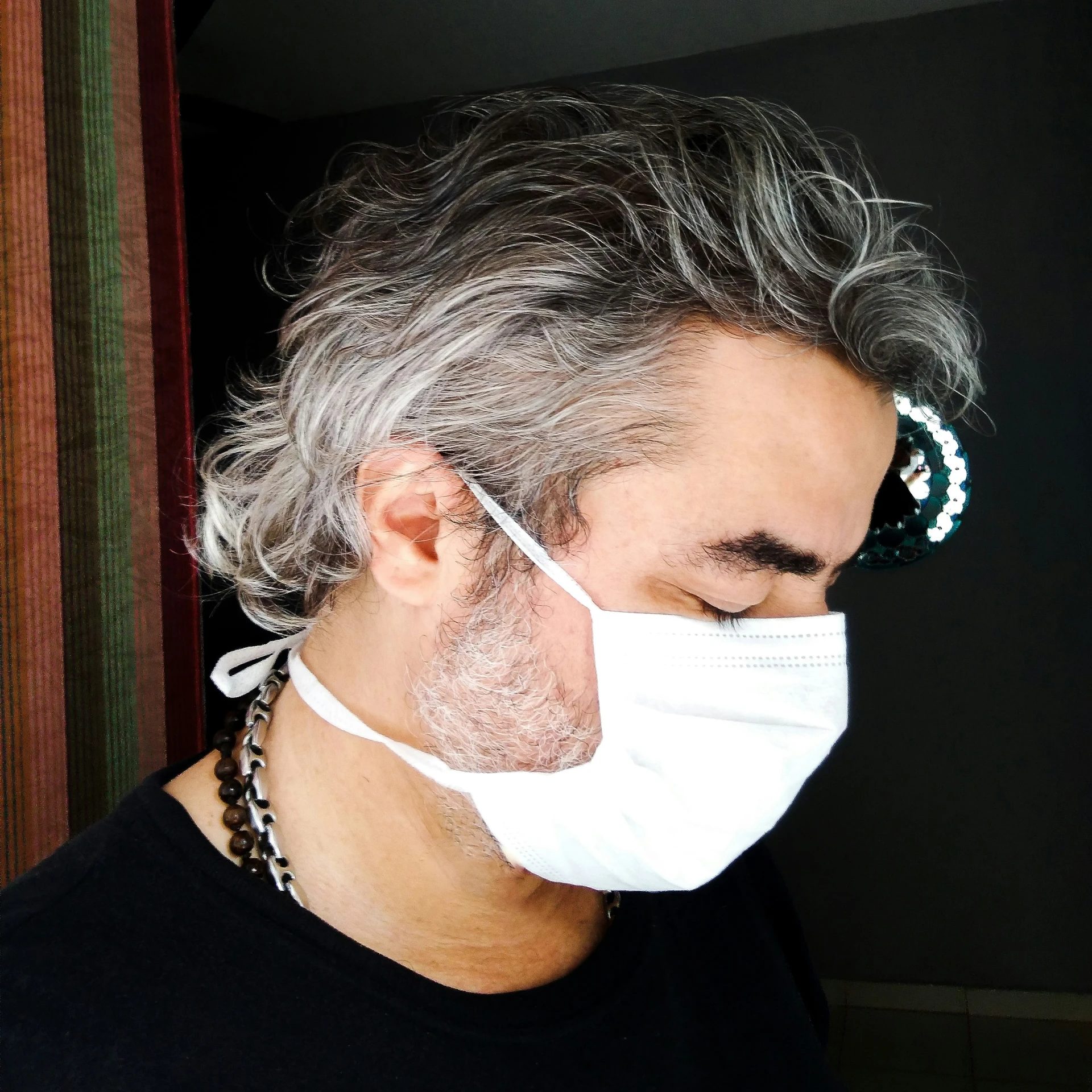 man in a black t - shirt wearing a mask and his hair is gray