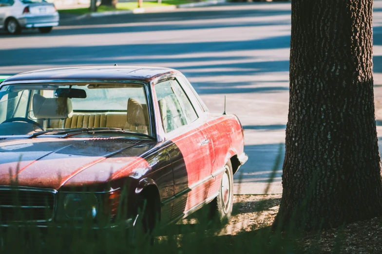 an old rusted red car parked next to a tree