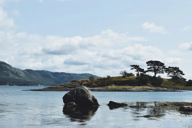 large rock in the water with hills in the background