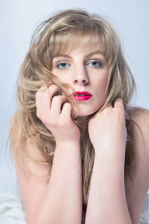 young blond woman posing with her arms near her face