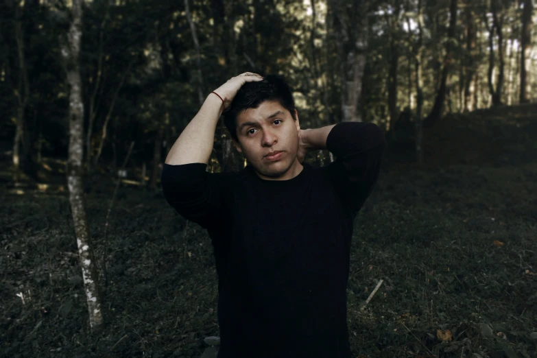 a man wearing black standing in the forest posing for the camera