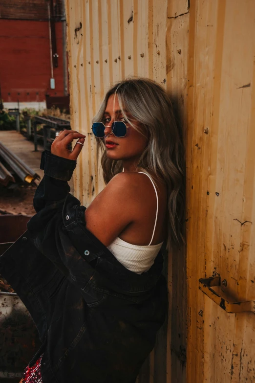 a woman wearing sunglasses leaning against the side of a building