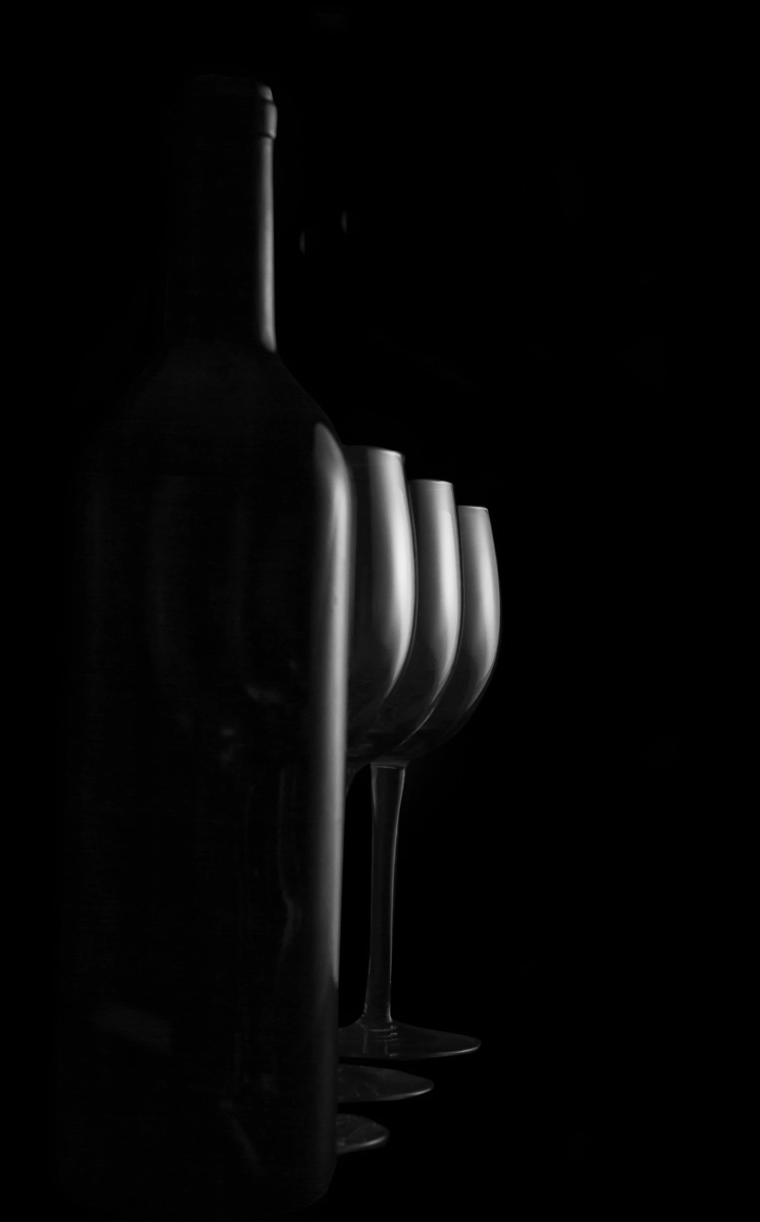 black and white pograph of empty wine glasses in front of bottles