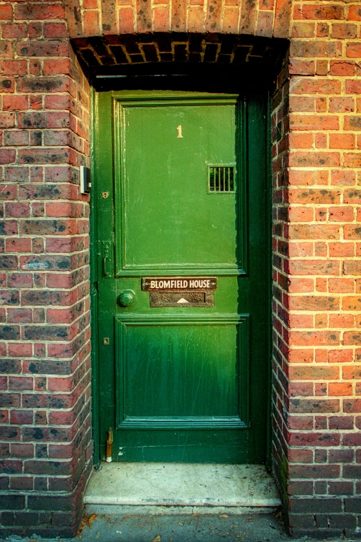 a green door with a sign on it by some brick