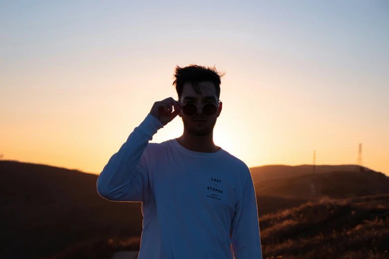 a man standing in front of the sun with the sun peeking through his sunglasses