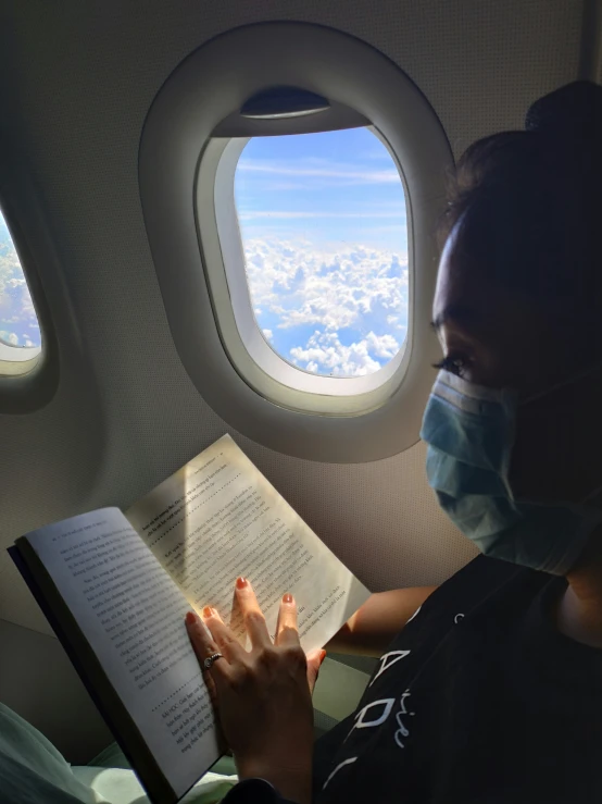 a woman is sitting down reading while wearing a mask