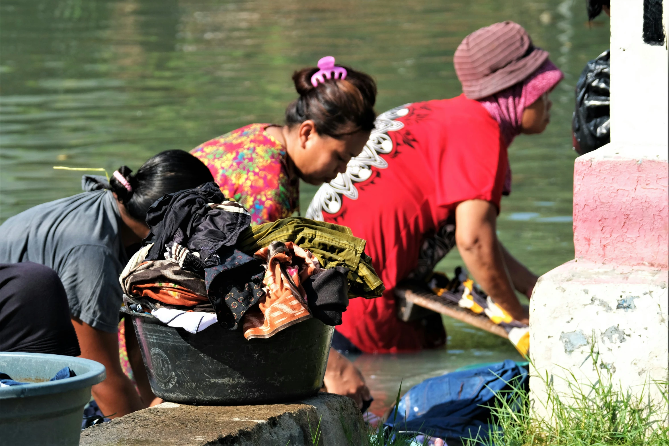 two women washing clothes and other clothing by the water