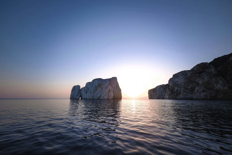 the sun shines through two large rocks on top of a lake