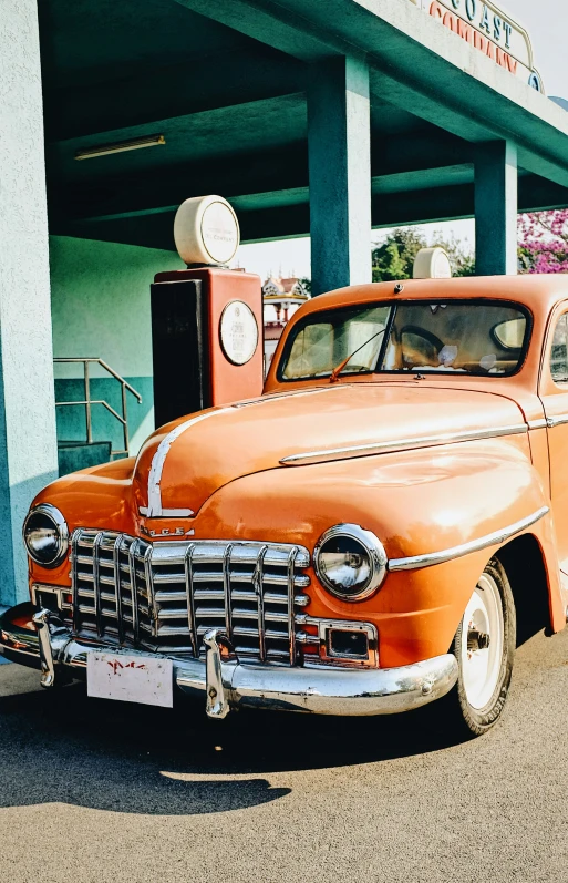 a classic orange car is parked in front of an old gas station