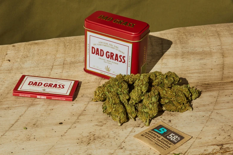 a small tin of weed next to a small pack of dad grass